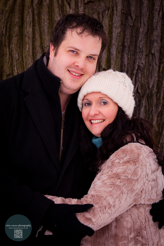 Couple embracing. Facing camera, smiling, resting against a tree